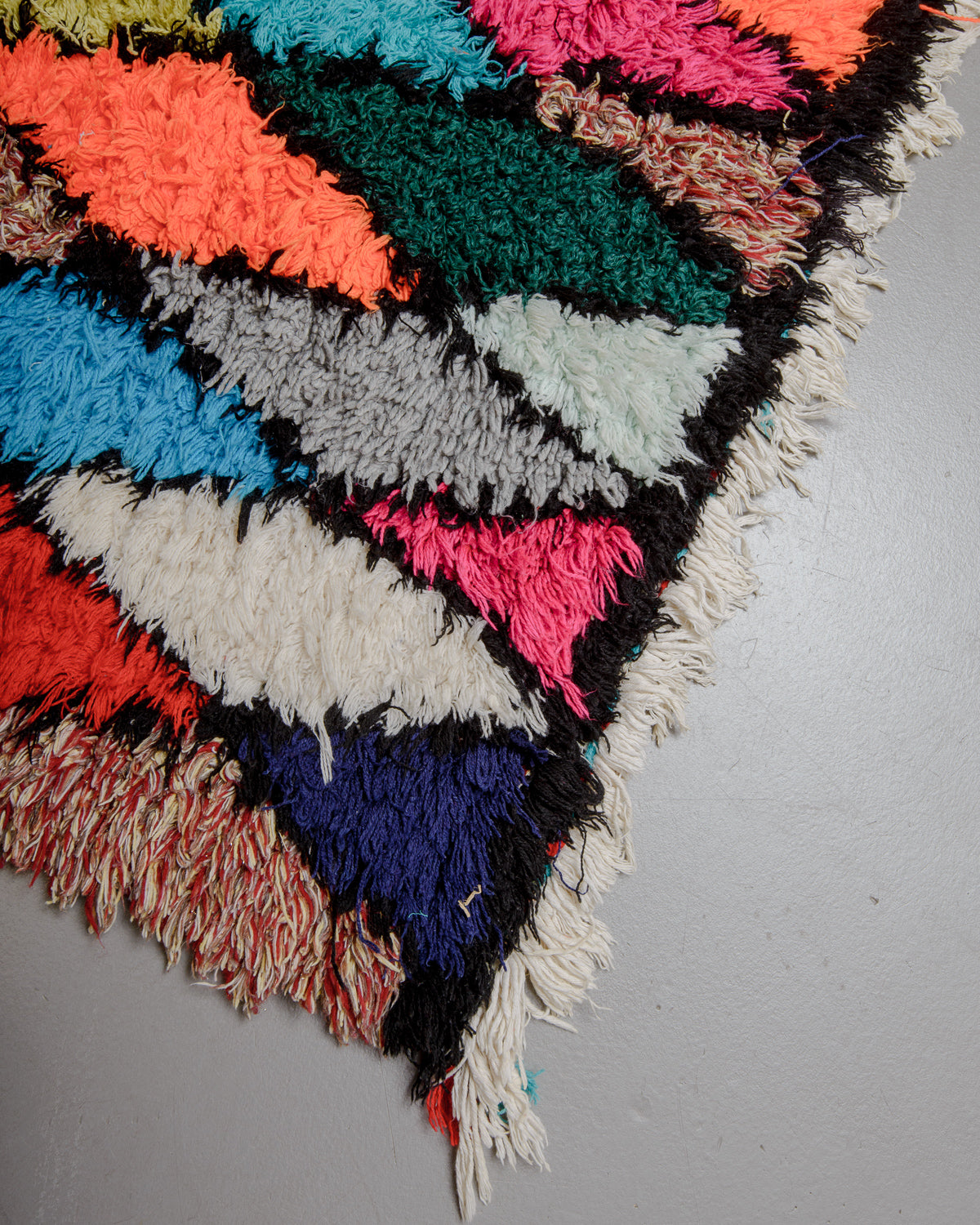 Corner of rust red and blue rug with multicoloured cotton tassels.