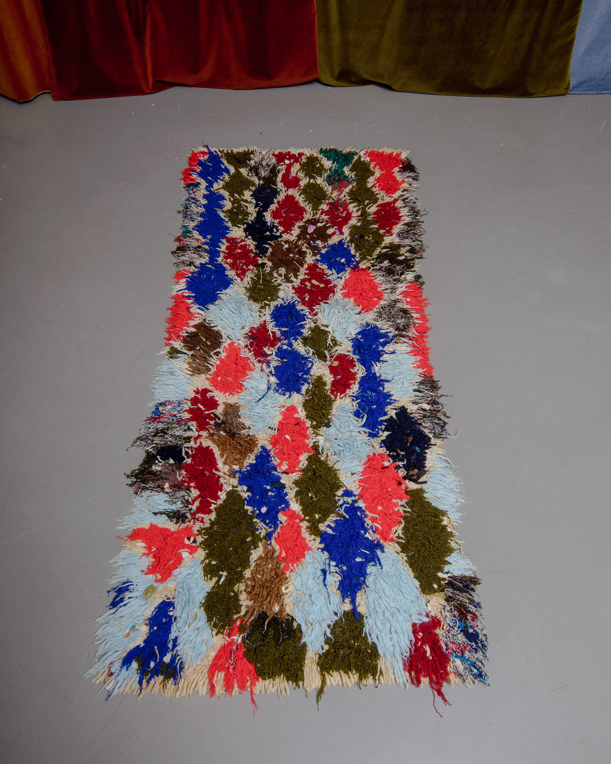 Vintage Berberlin boucherouite runner rug  on grey floor in front of velvet curtain. 