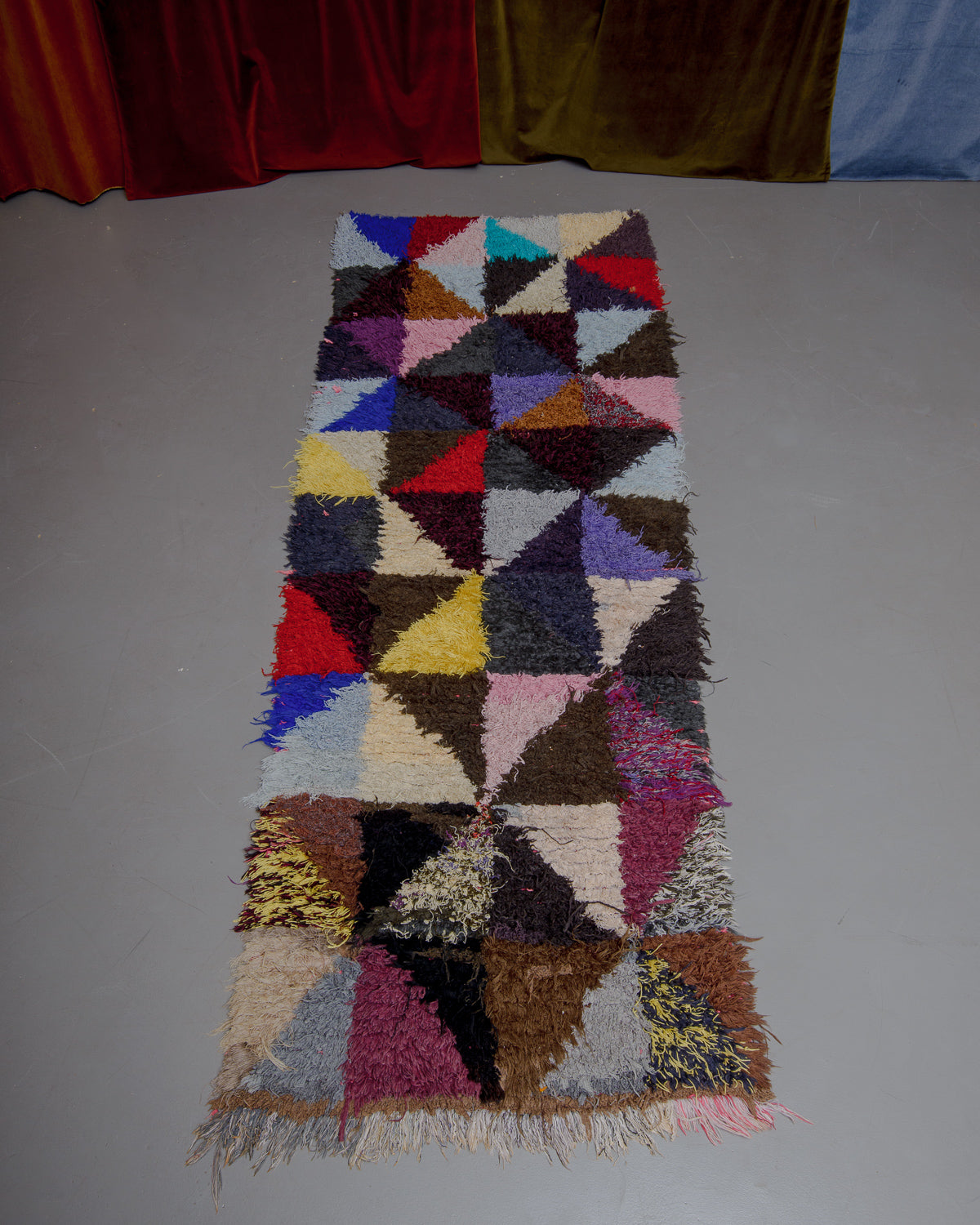 Vintage Berberlin boucherouite runner rug on grey floor in front of velvet curtain. 