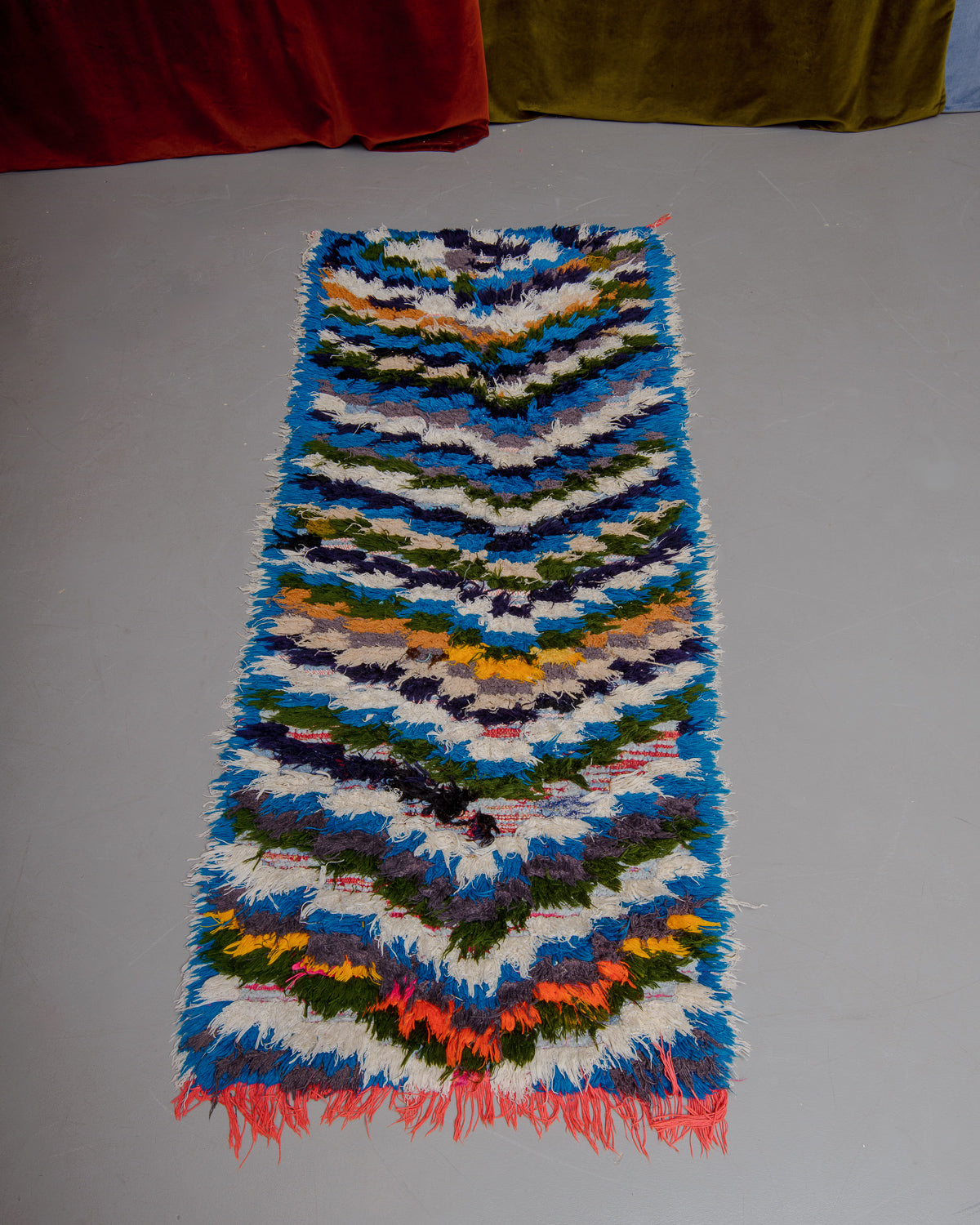 Vintage Berberlin boucherouite runner rug on grey floor in front of velvet curtain. 