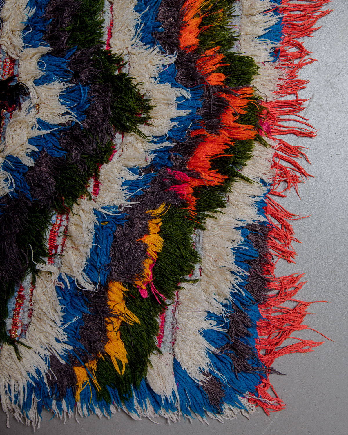 Corner of boucherouite rug with red, green, orange, blue and white cotton.