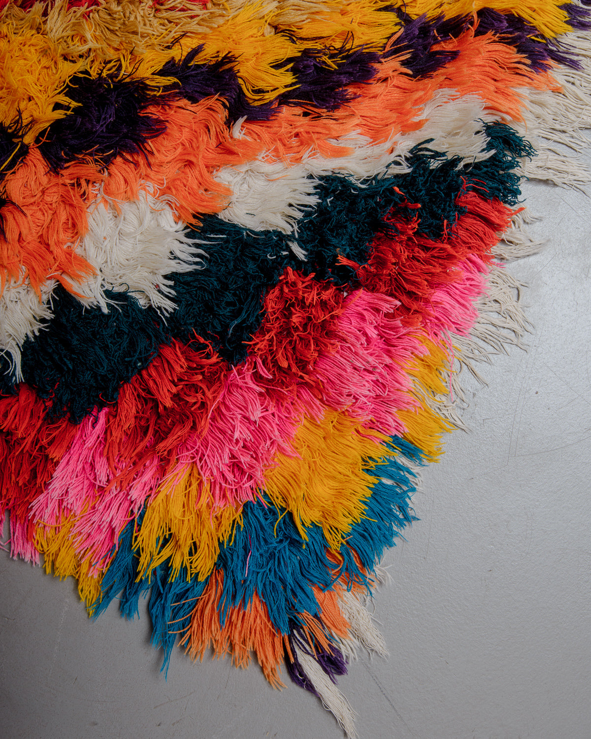 Corner of boucherouite rug with red, pink orange, teal and white cotton.