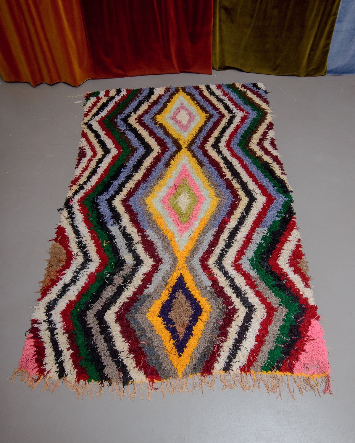 Boucherouite rug on grey floor in front of velvet curtains.