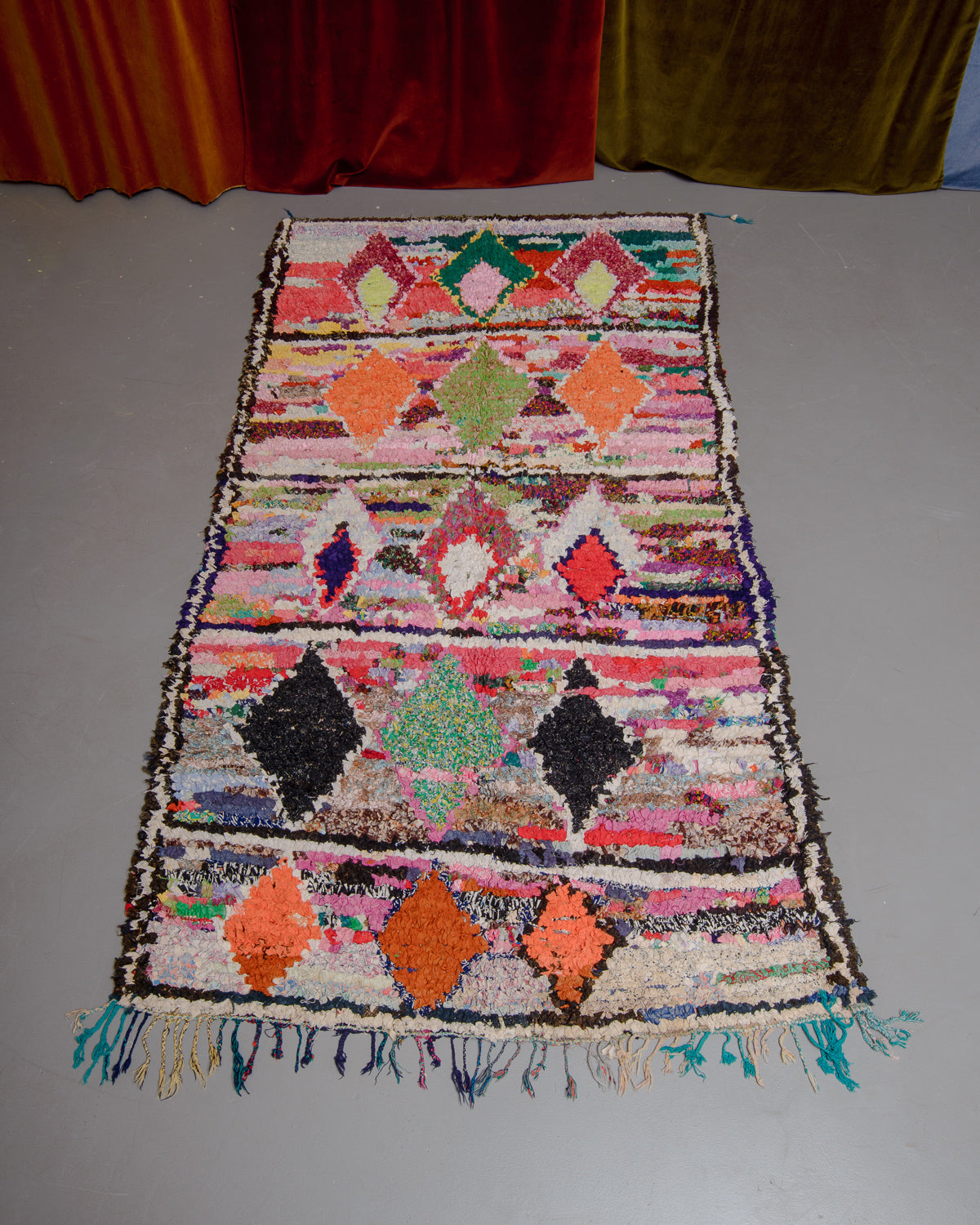 Boucherouite rug on grey floor in front of velvet curtains.