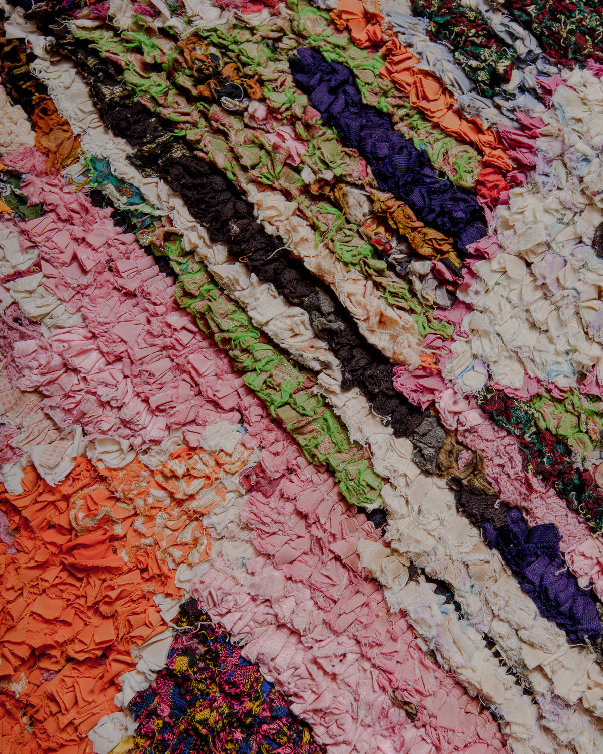 Close up of surface of Boucherouite rug in varying shades of pink, orange and green.