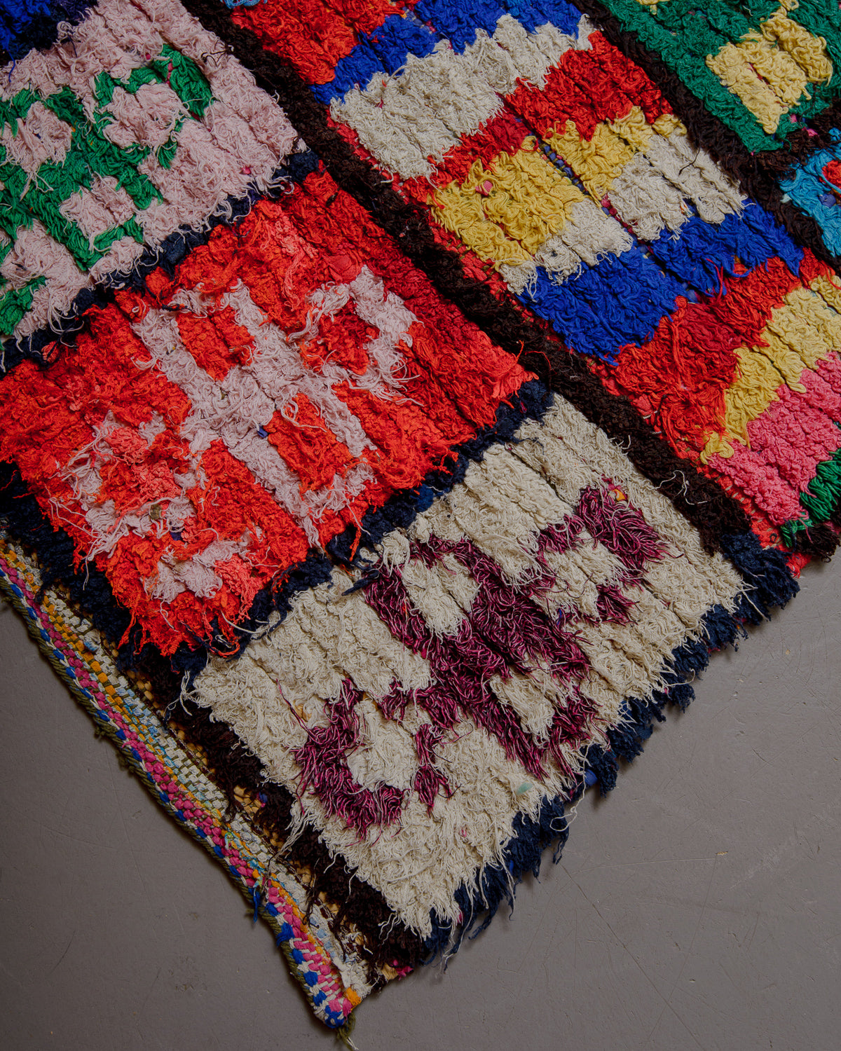 Corner of Boucherouite rug with bold primary colours on grey floor.