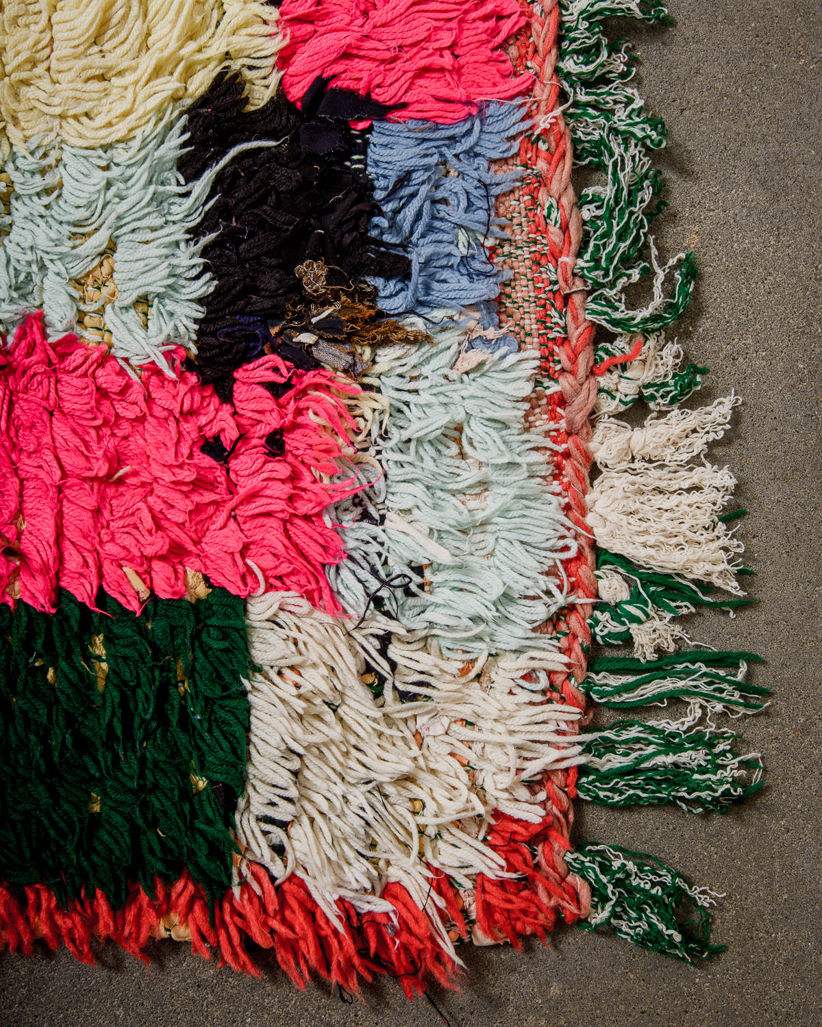 Colourful textured rug with a mix of bright and neutral colors on a concrete surface.