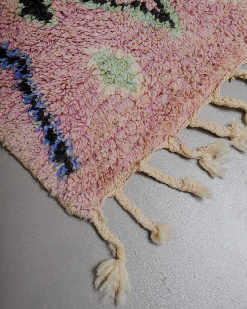 Corner of mauve wool rug with natural wool tassels. 