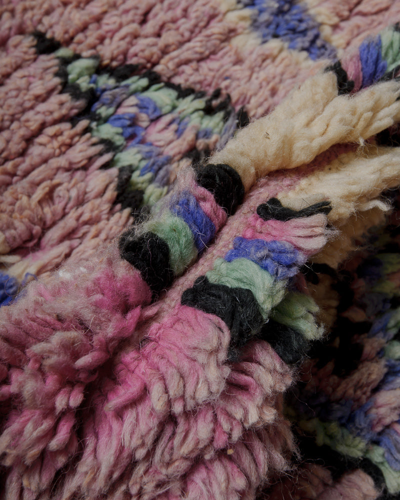 Close up of mauve wool rug with design elements in turquoise, blue, black and cream.