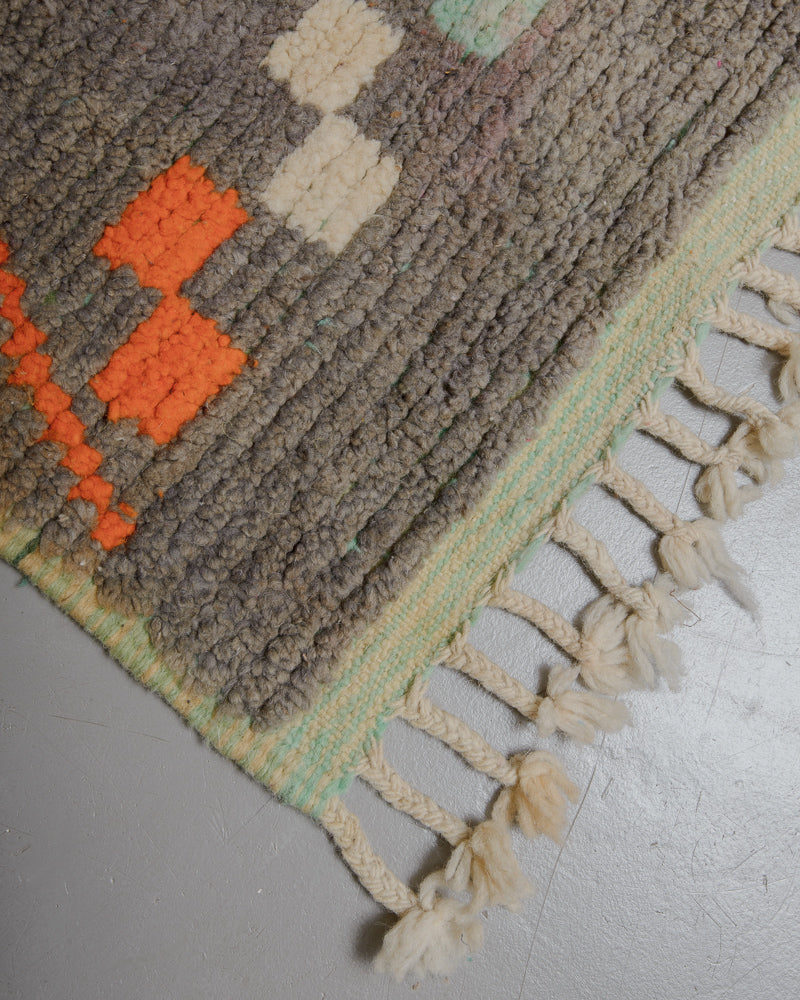 Corner of warm grey wool rug with natural wool tassels and turquoise woven edge. 