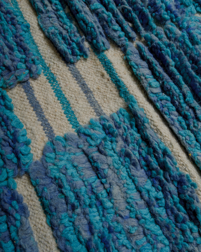 Surface of wool rug with blue pile and striped woven areas. 
