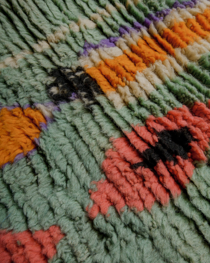 Surface of wool rug made of shades of turquoise, orange, purple and coral.