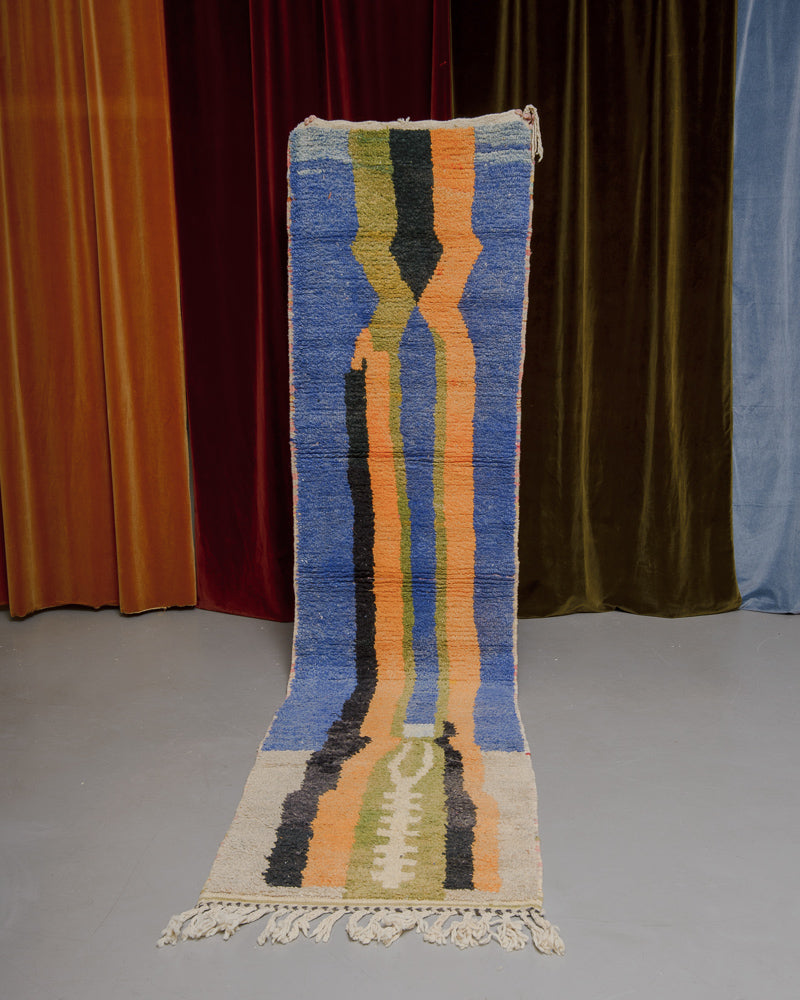 Vintage Berberlin runner rug being held up in front of a velvet curtain. 