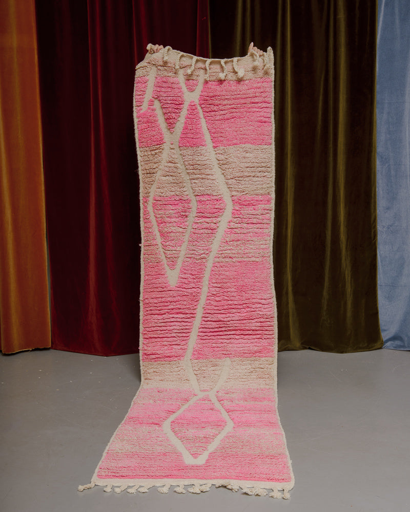 Vintage Berberlin runner rug being held up in front of a velvet curtain. 