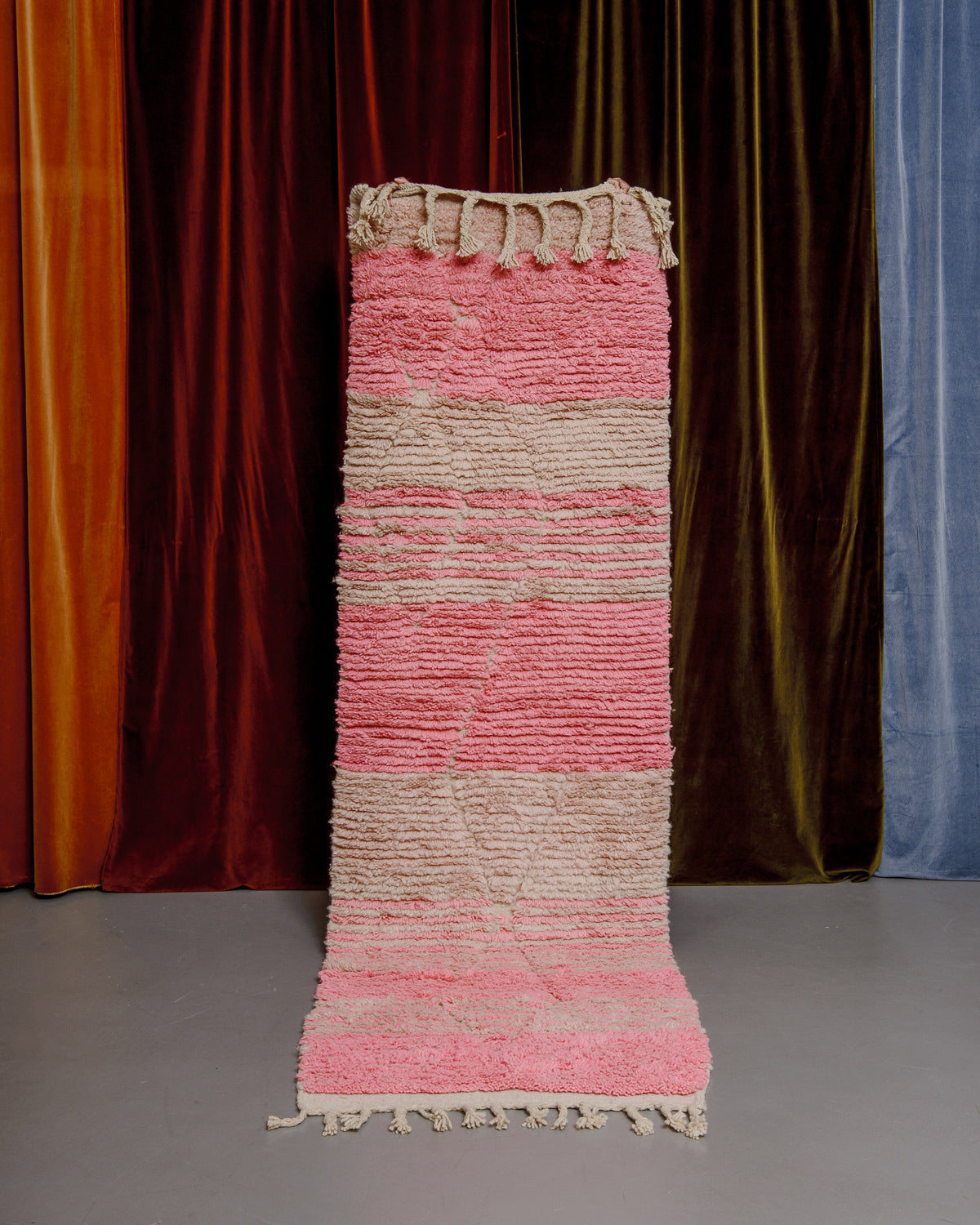 Vintage Berberlin runner rug being held up in front of a velvet curtain. 