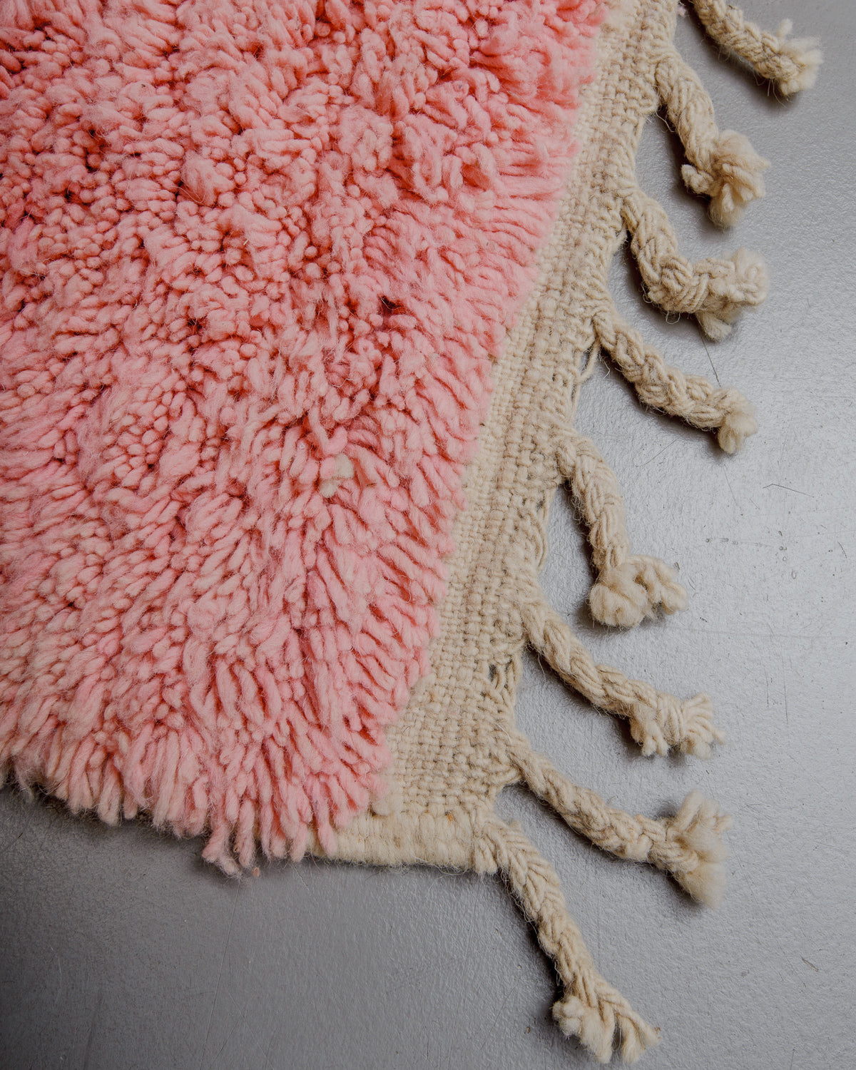 Corner of rose coloured wool rug with natural wool tassels. 
