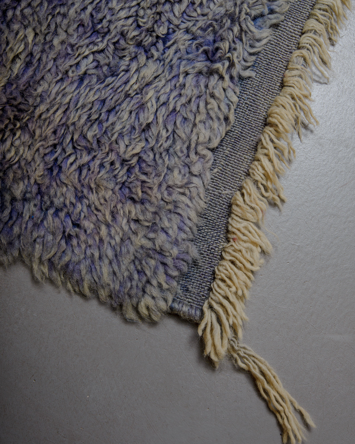 Corner of vintage wool rug with textured pile and flat woven edge with natural wool tassels. 