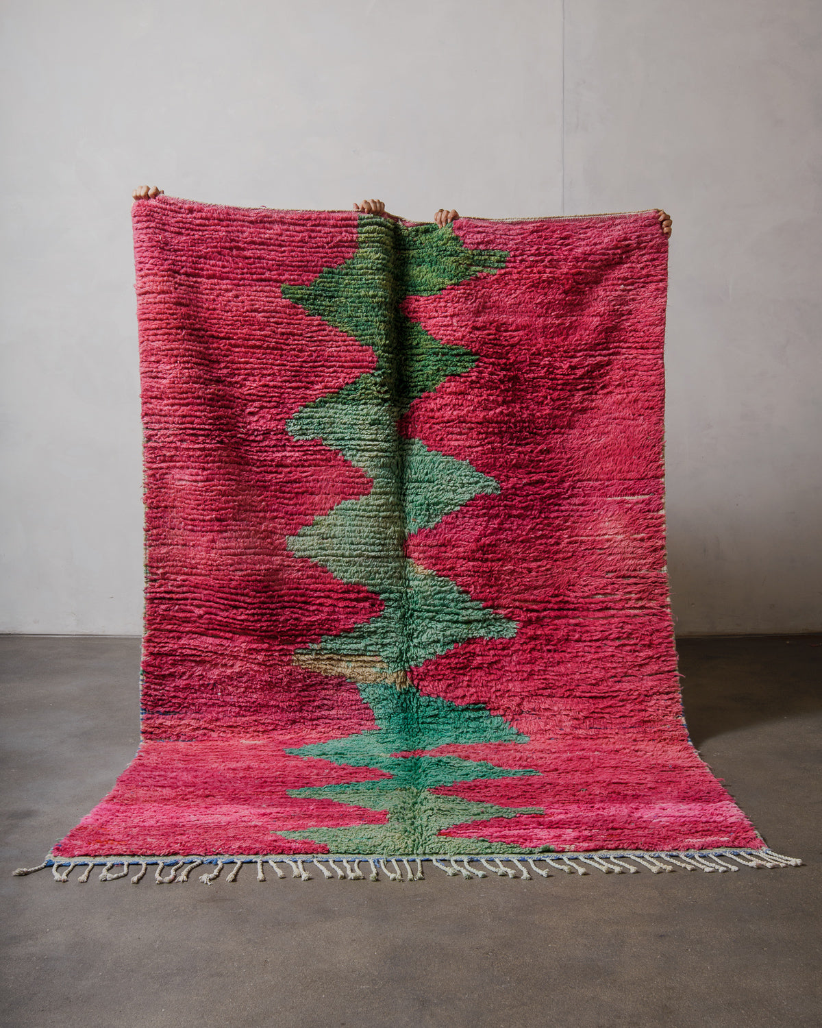 Pink and green woven rug on a plain background