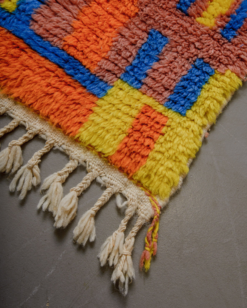 Corner of rug with yellow, orange and blue pattern and natural wool tassels. 