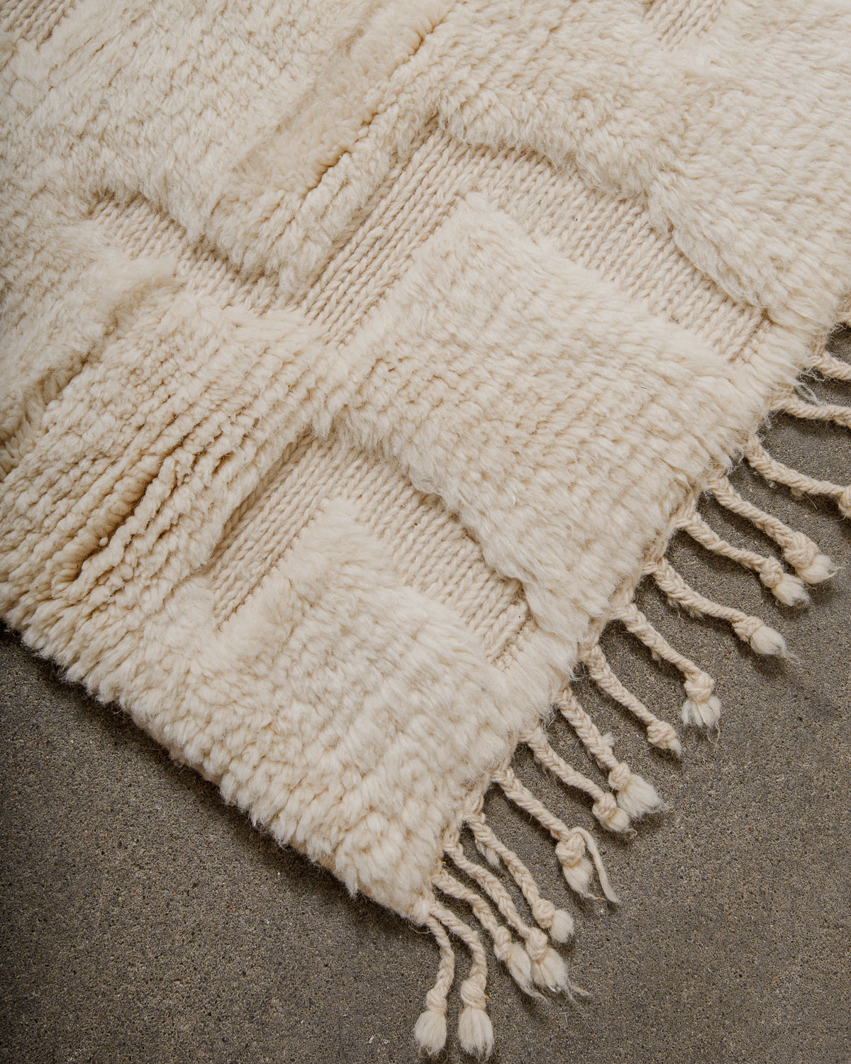 Close-up of a textured cream wool rug with fringes on a neutral background