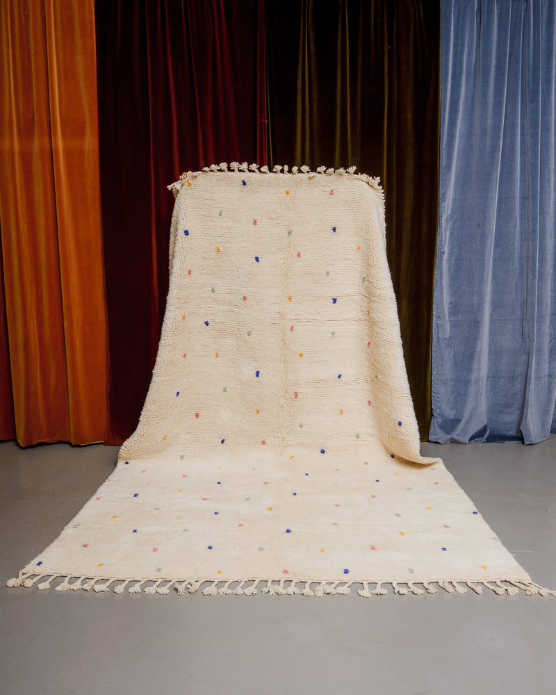 Cream wool rug with colourful polka dots in front of velvet curtains.