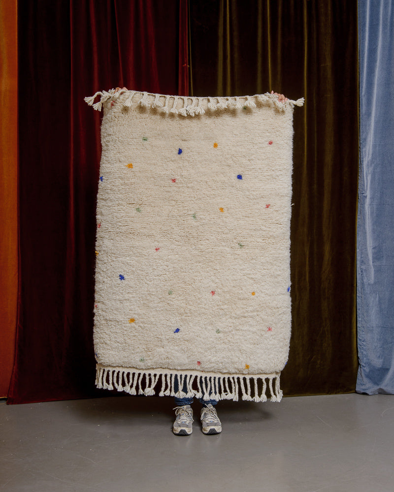 Berberlin Finest dotted rug being held up in front of velvet curtains. 