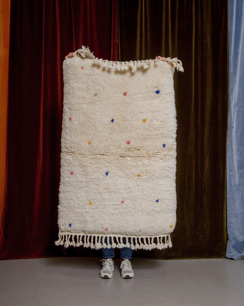 Berberlin Finest dotted rug being held up in front of velvet curtains. 