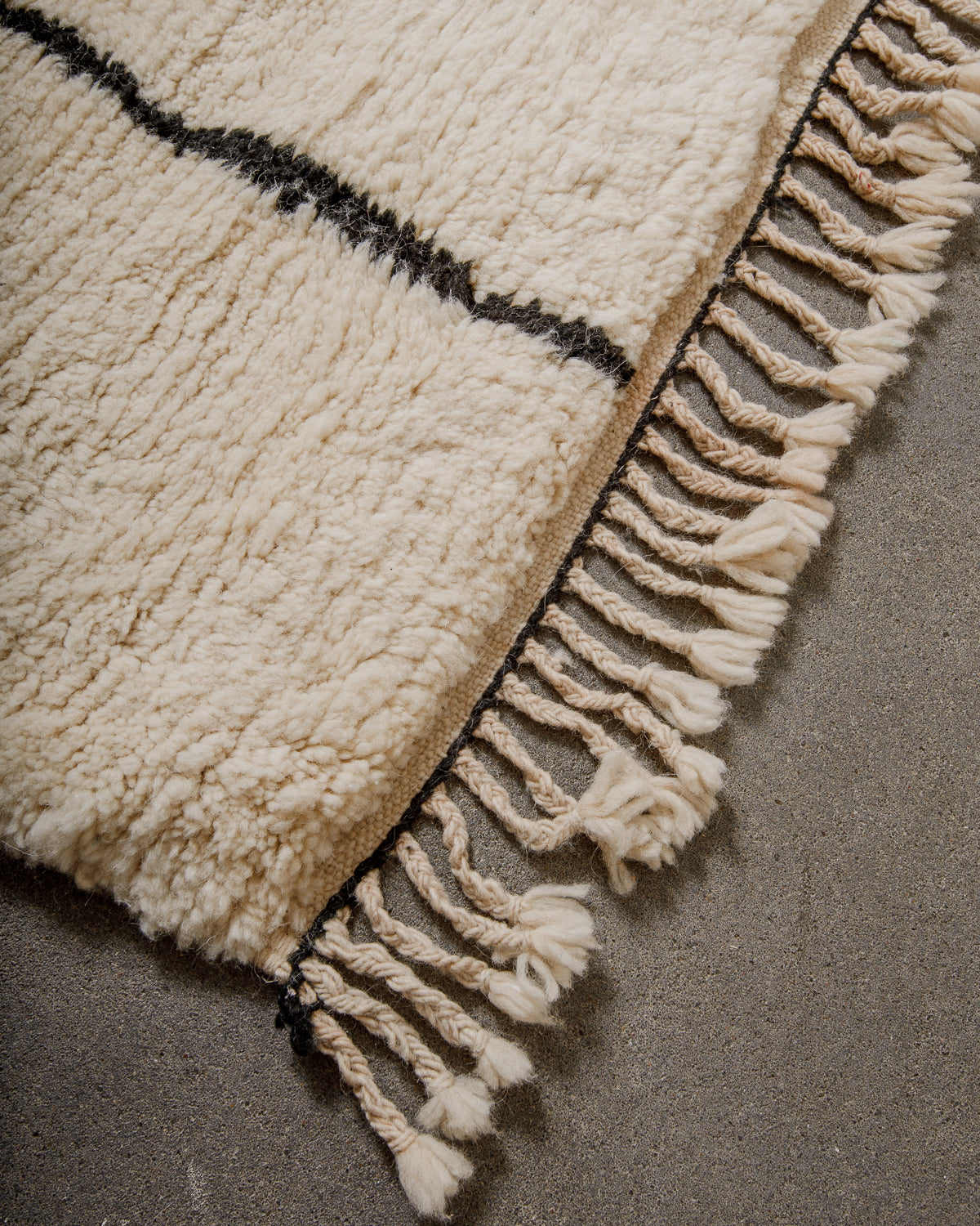 Close-up of a textured wool rug with fringes on a neutral background
