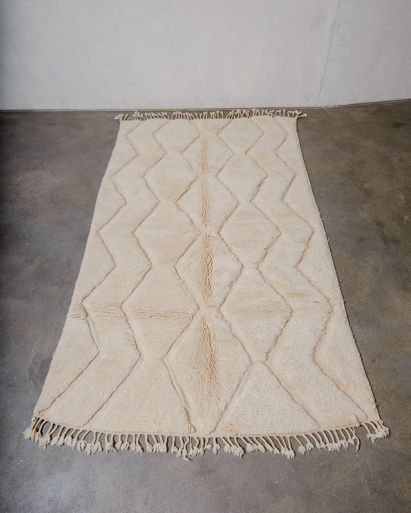 Cream wool woven rug with diamond pattern on a concrete floor