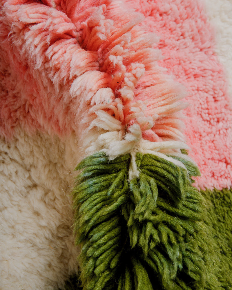 Close up of wool rug with thick pile in green, pink and cream.