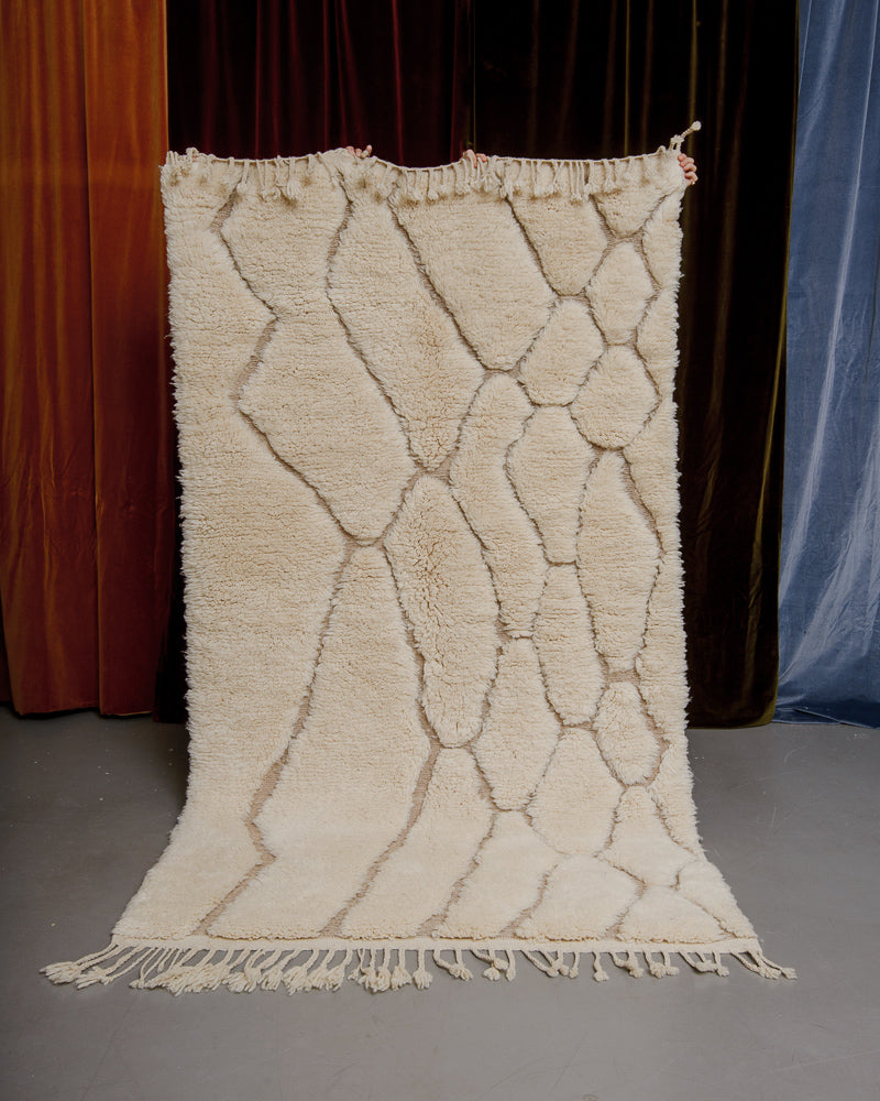 Cream Berberlin Finest rug being held up in front of velvet curtains.