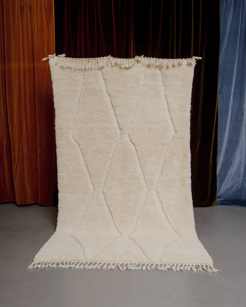 Cream Berberlin Finest rug being held up in front of velvet curtains.