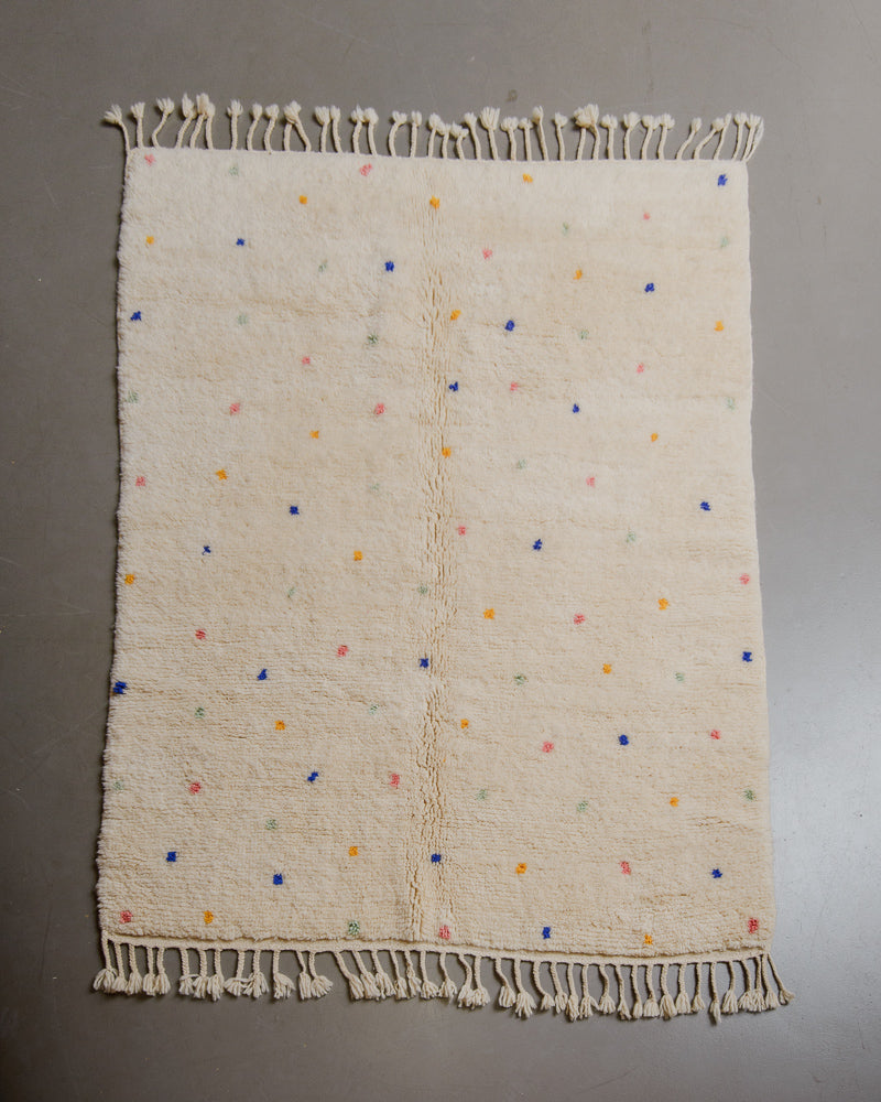 Cream wool rug with colourful polka dots on grey floor. 