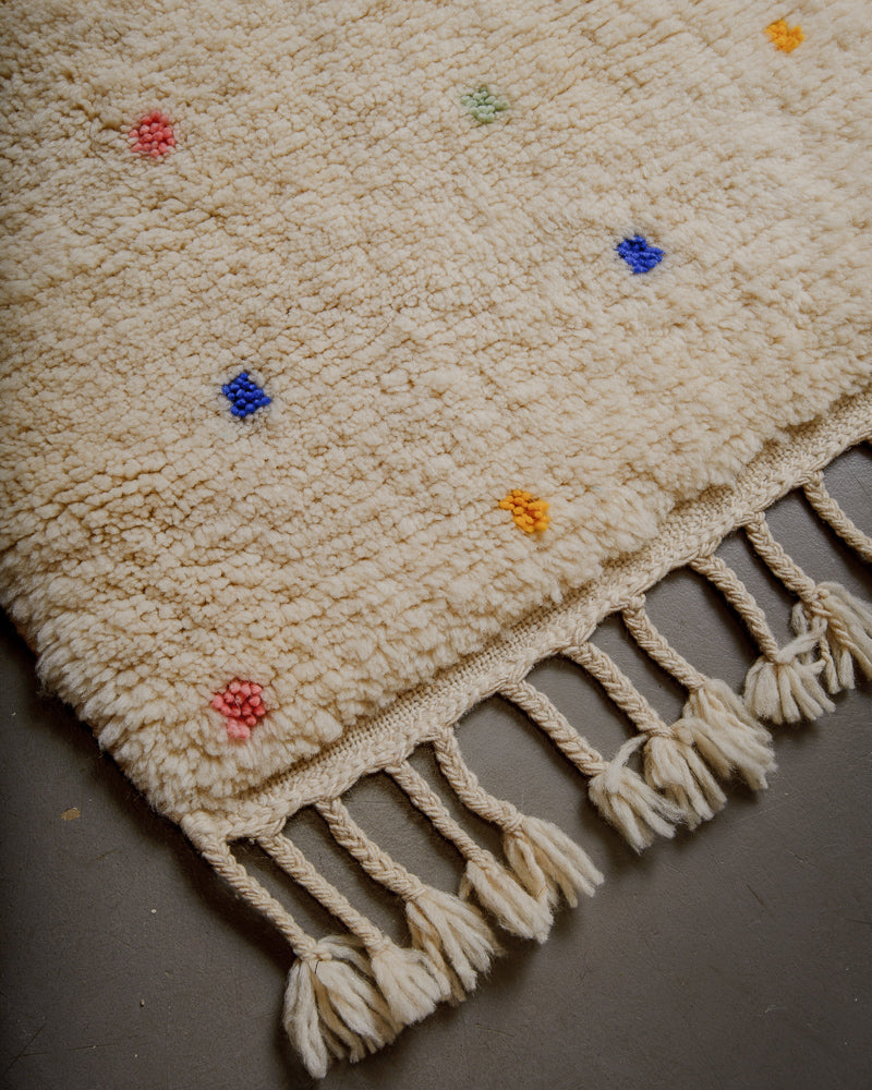 Corner of cream wool rug with colourful polka dots and natural wool tassels.