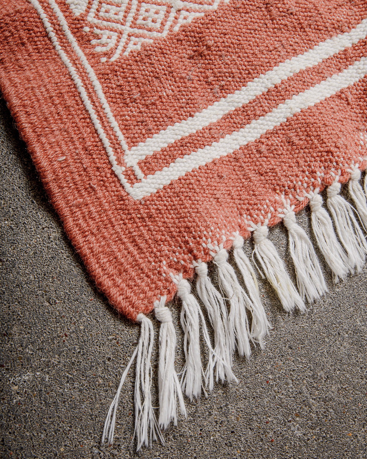 Corner of Vintage Kelim Rug in shades of terracotta and white, finished with white cotton tassels on each end. 