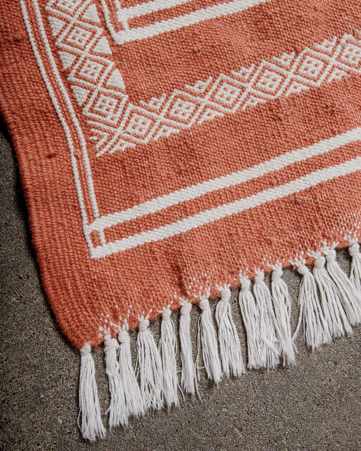 Corner of Vintage Kelim Rug in shades of terracotta and white, finished with white cotton tassels on each end. 
