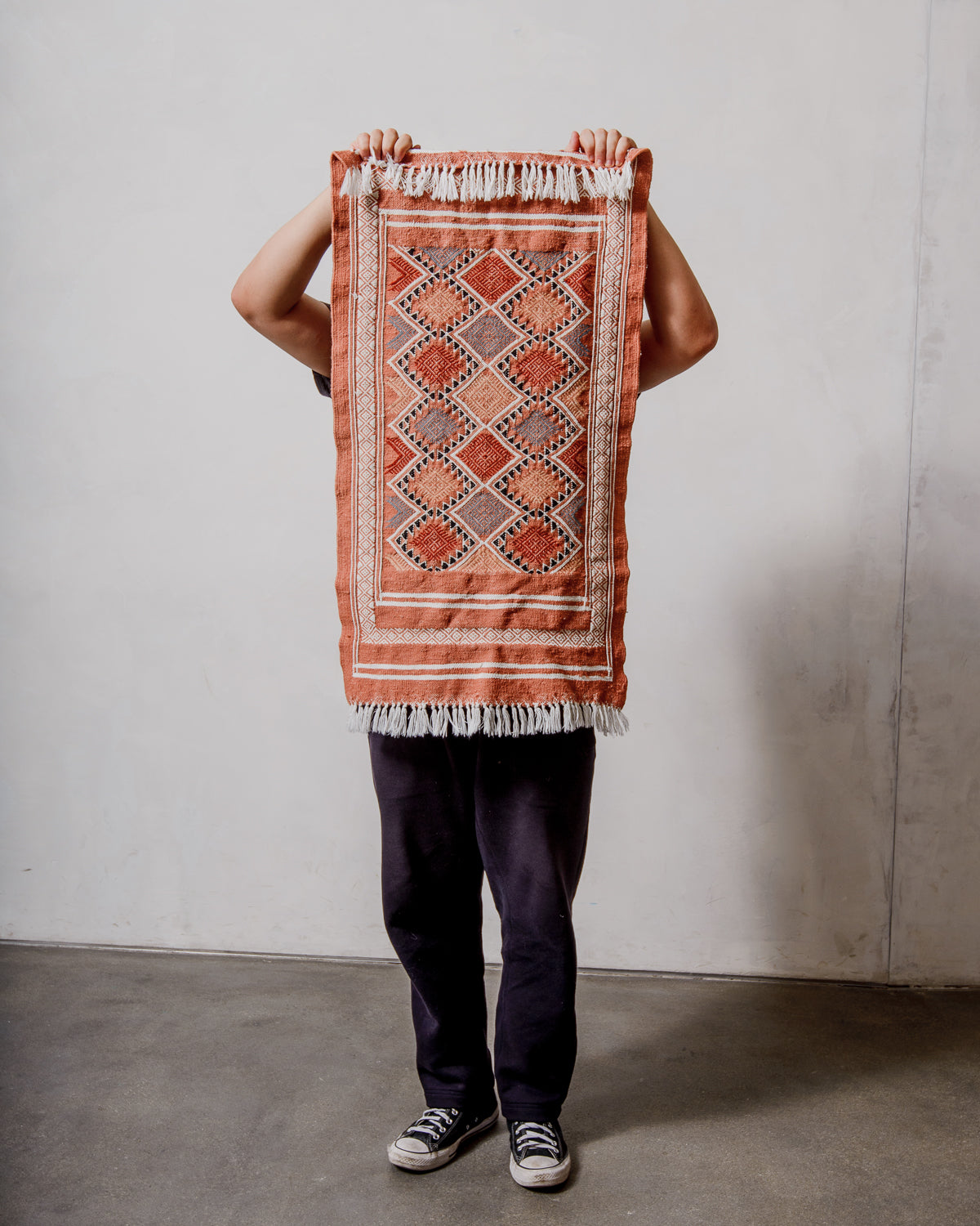 Small Berberlin Vintage Kelim Rug in shades of terracotta and white being held up in front of a white wall. 