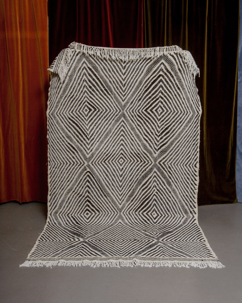 black and white kelim rug held up in front of velvet curtains