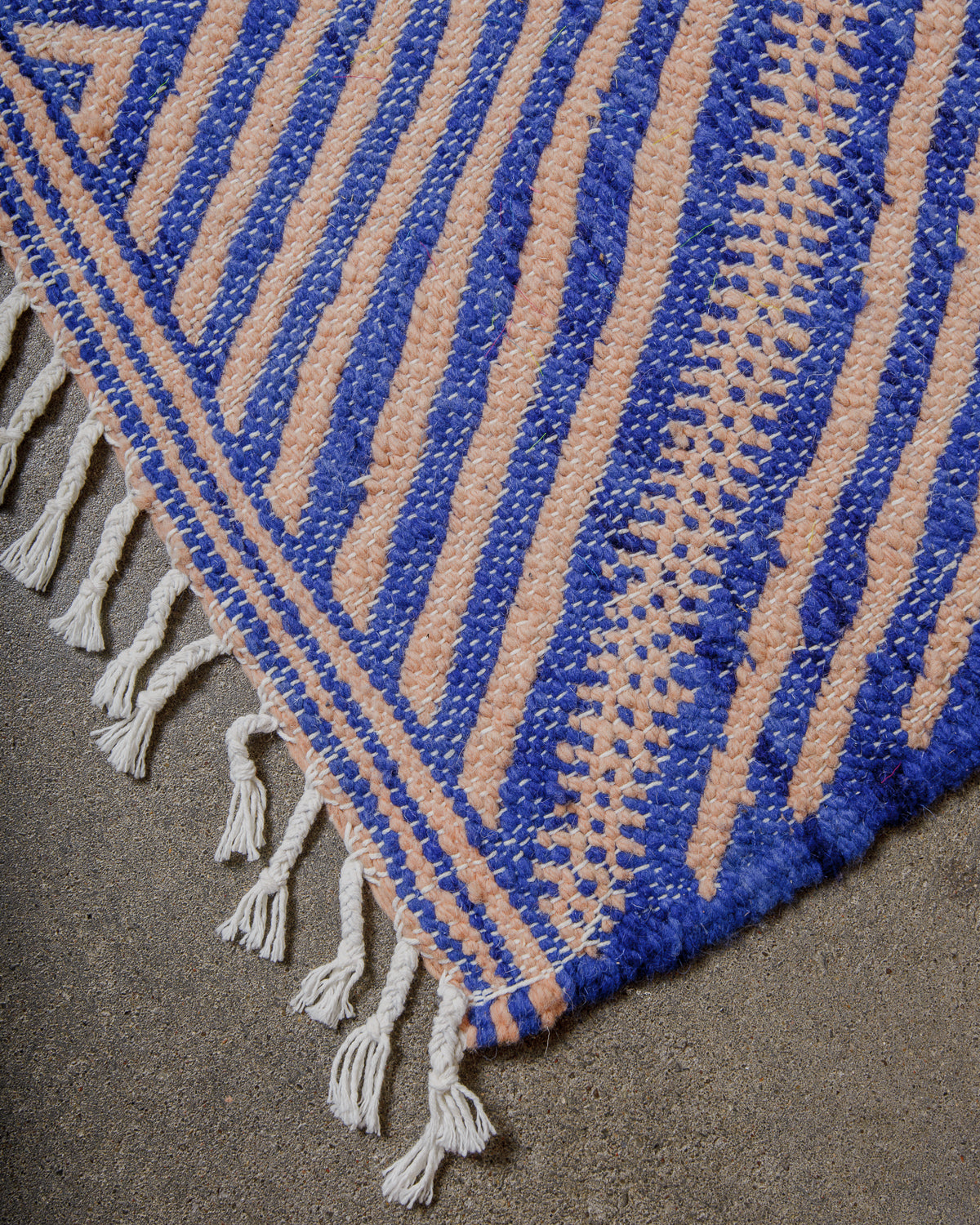Corner of blue and rose coloured kelim with white cotton tassels.
