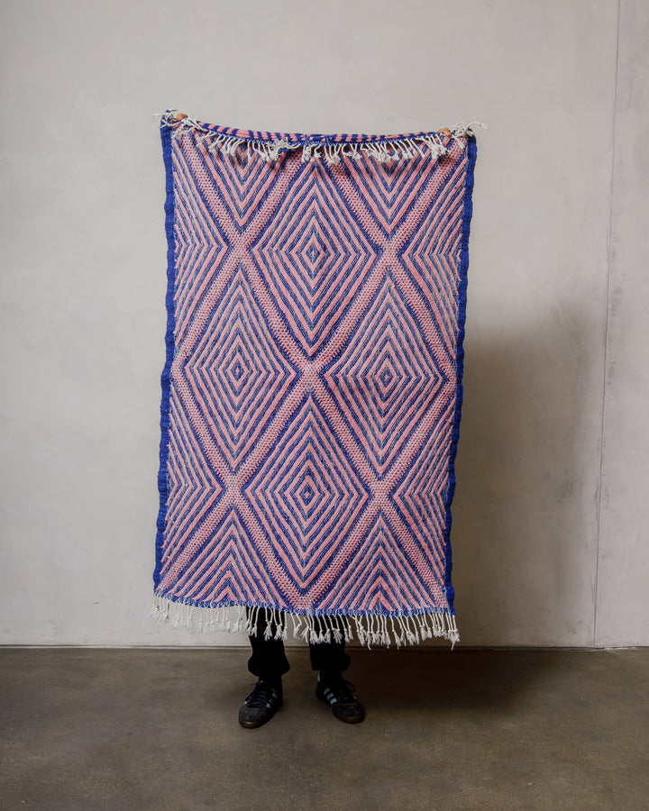 Person holding a blue and pink patterned Berberlin Kelim rug against a plain background