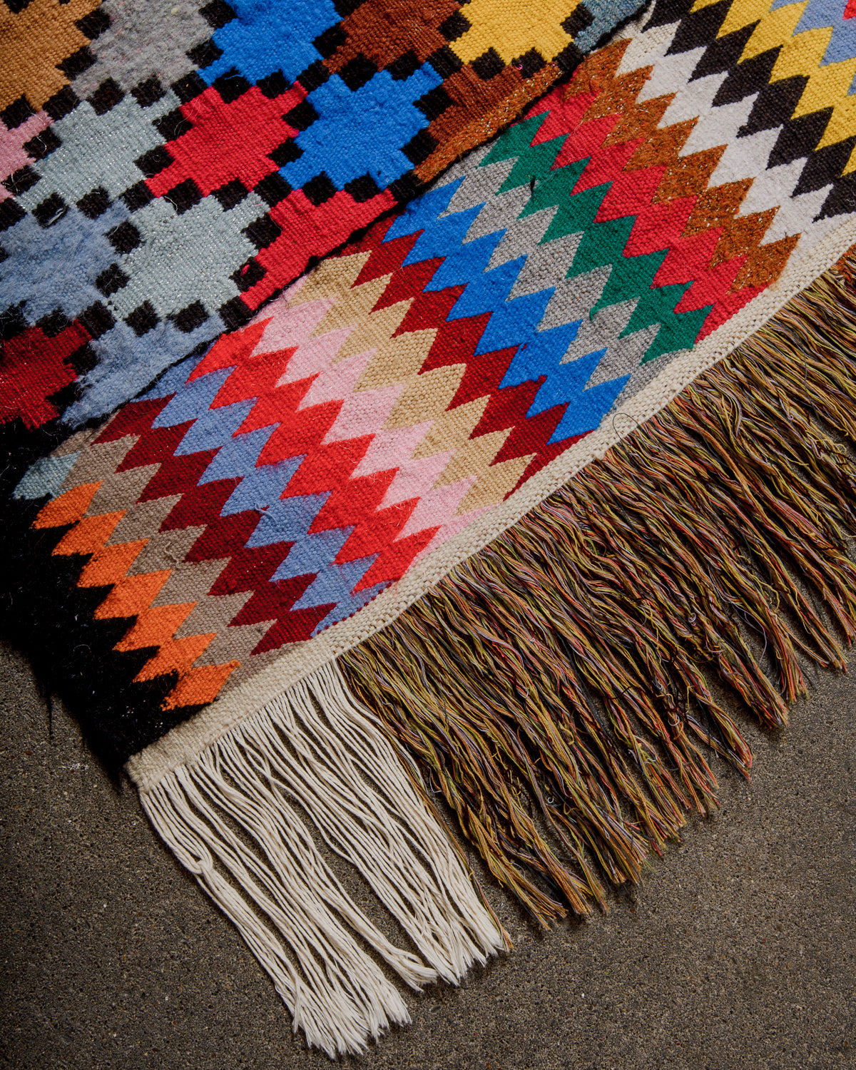 Corner of Vintage Kelim runner rug with a brightly coloured harlequin design and black borders, with long cotton tassels.