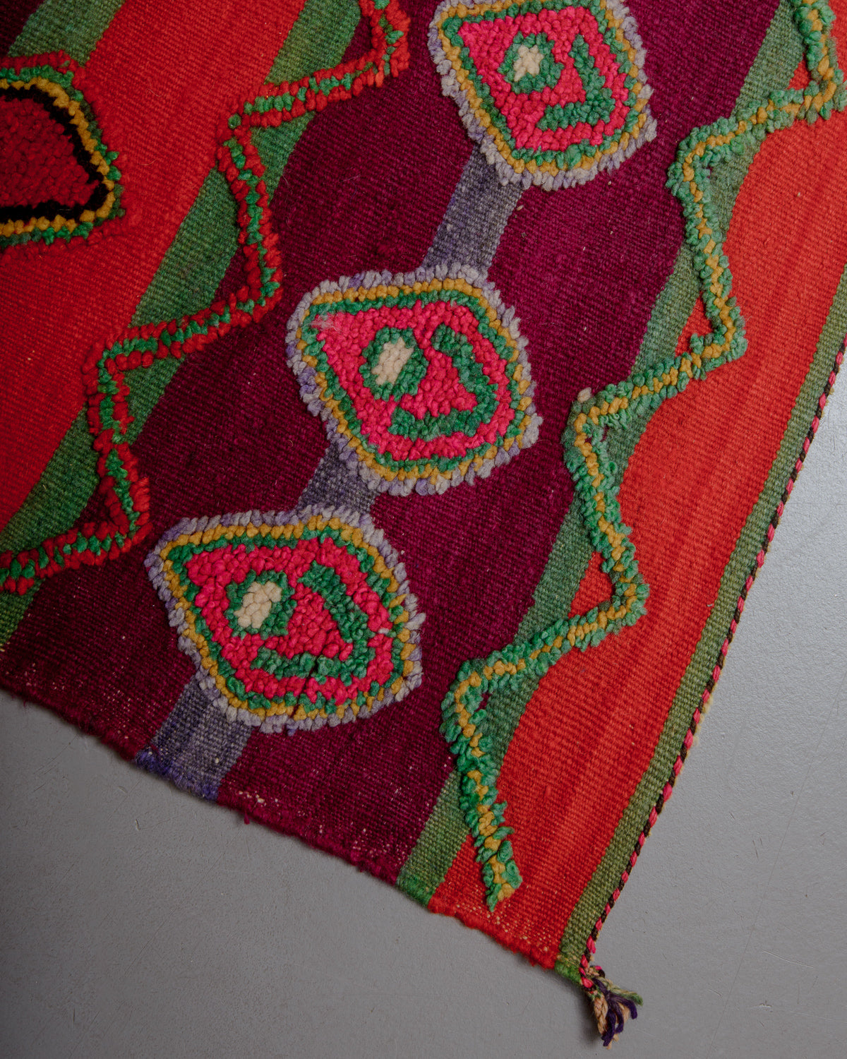 Corner of vintage kelim rug in red, green, burgundy and lavender wool.