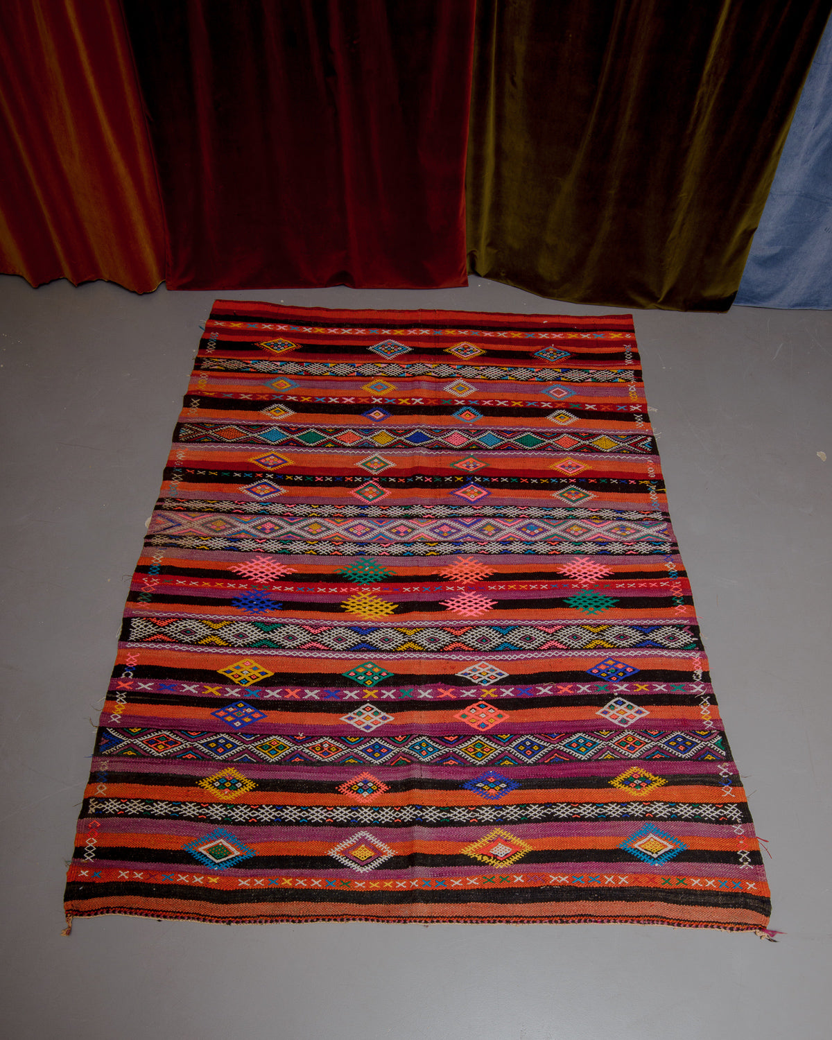 Vintage Kelim rug in bright orange, red, green and pink on grey floor.