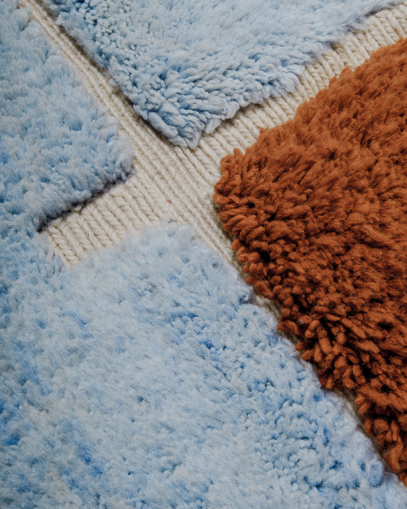 Close up of blue and brown mrirt rug with cream dente. 