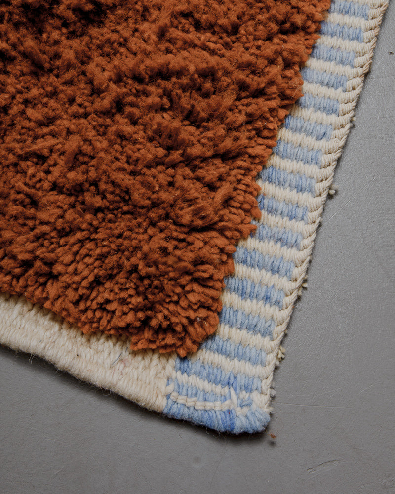 Corner of blue and brown mrirt rug with tightly woven edges.