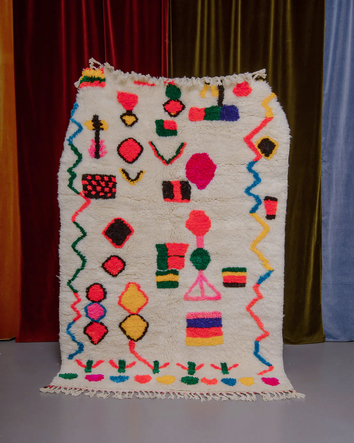 Berberlin Finest rug with a heavy cream pile and colourful design in cotton being held in front of velvet curtains. 