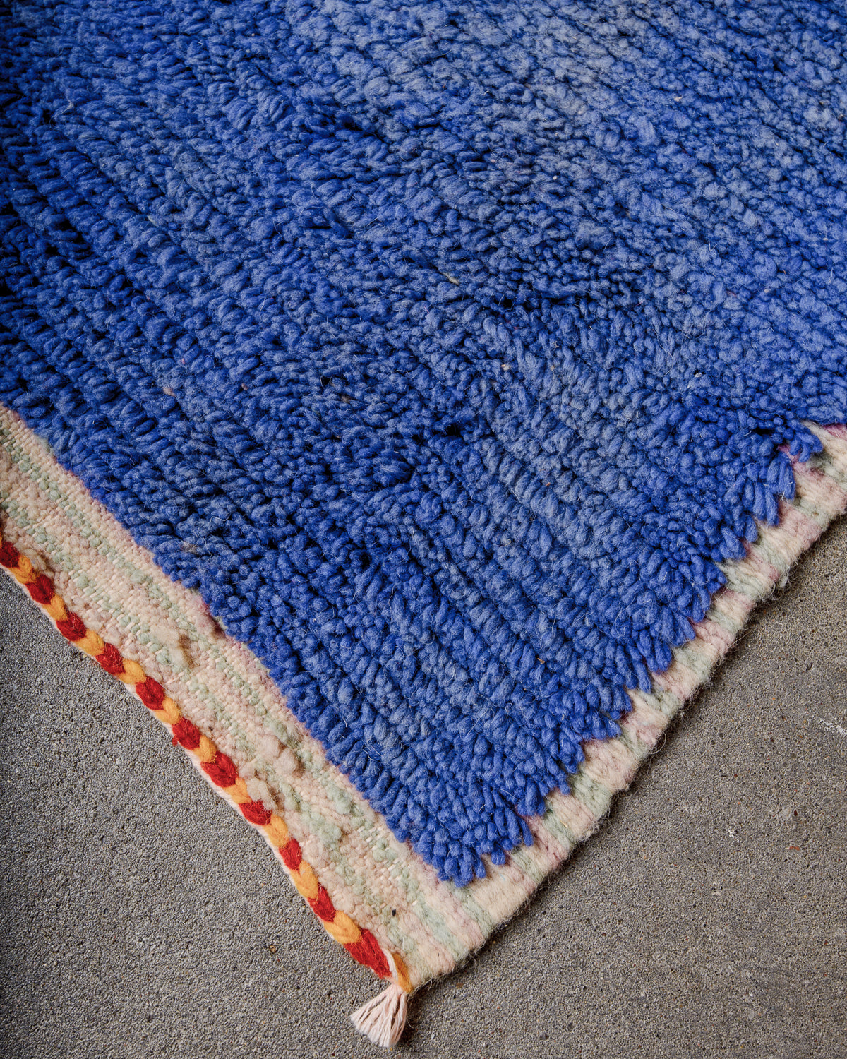 Corner of Berber runner rug with fluffy blue wool pile and tightly woven end. 