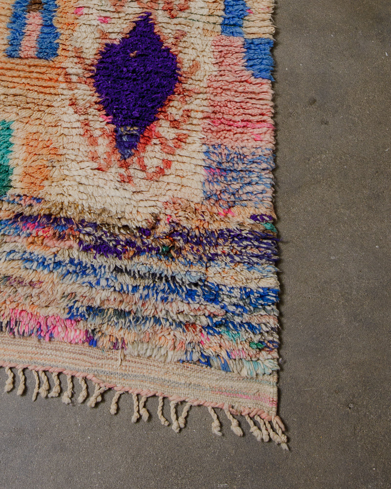 Corner of a runner rug with small wool tassels on a concrete floor. 