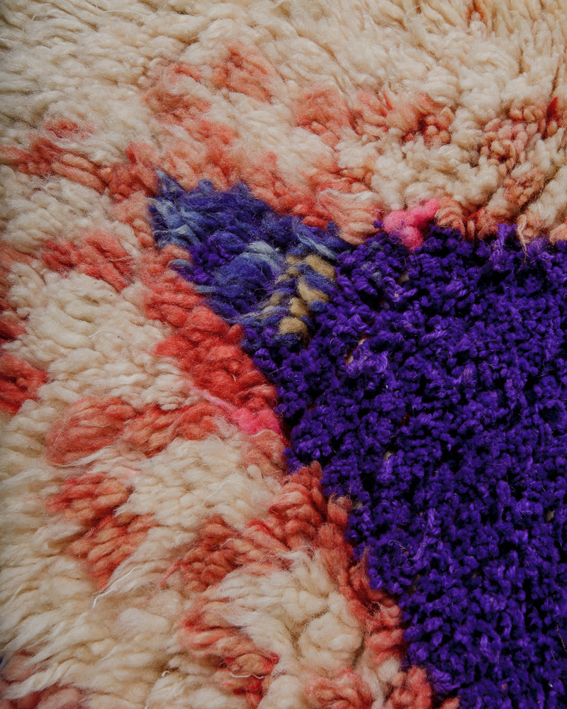 Close-up of a fluffy wool rug with a purple, beige and coral colours.