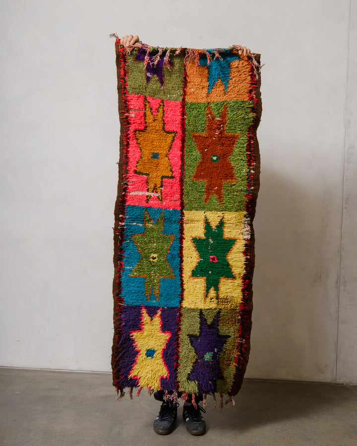 Vintage boucherouite rug being held up in front of a white wall. 